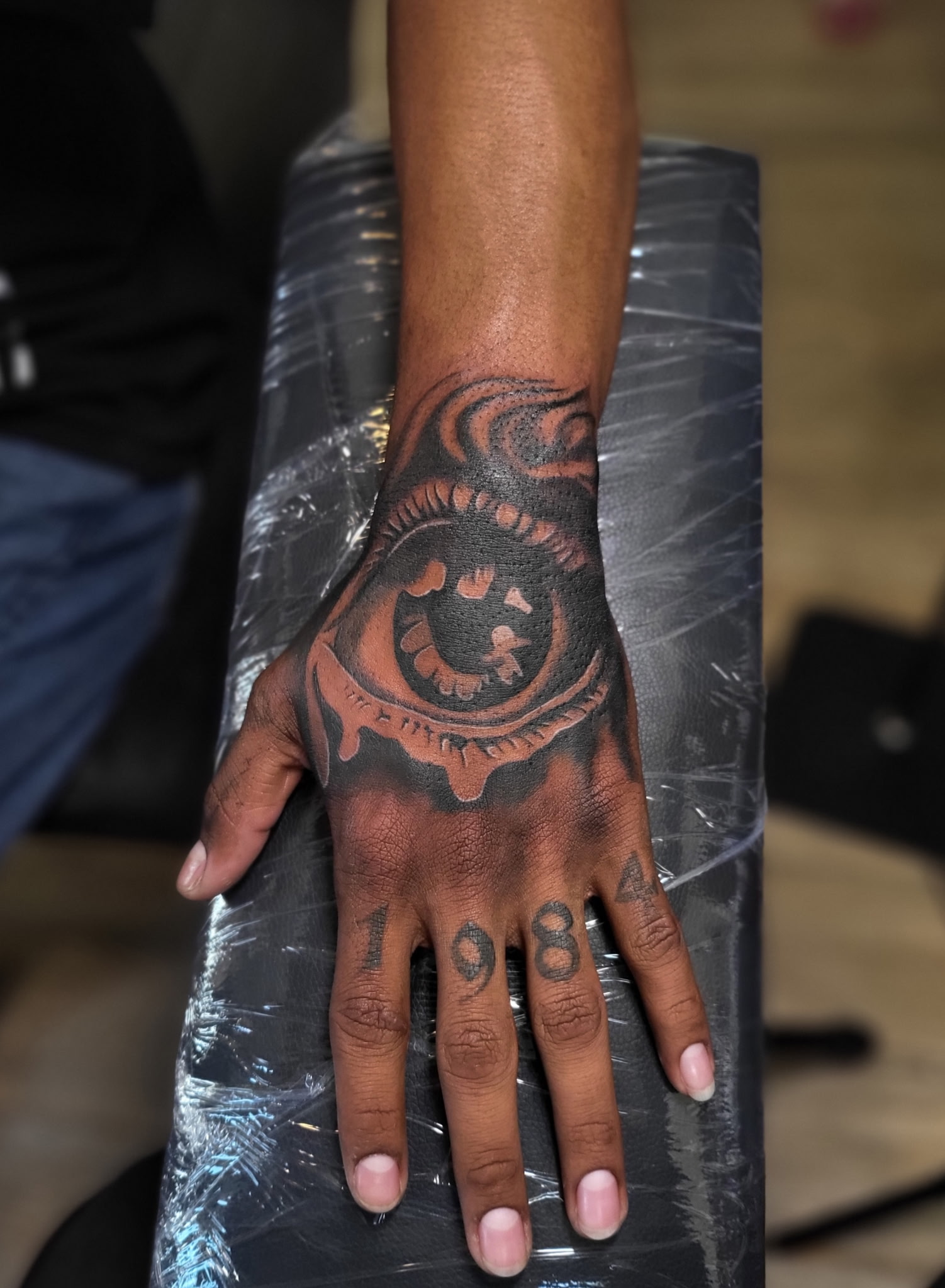 Realistic eye tattoo on the back of a hand with 1984 on the knuckles