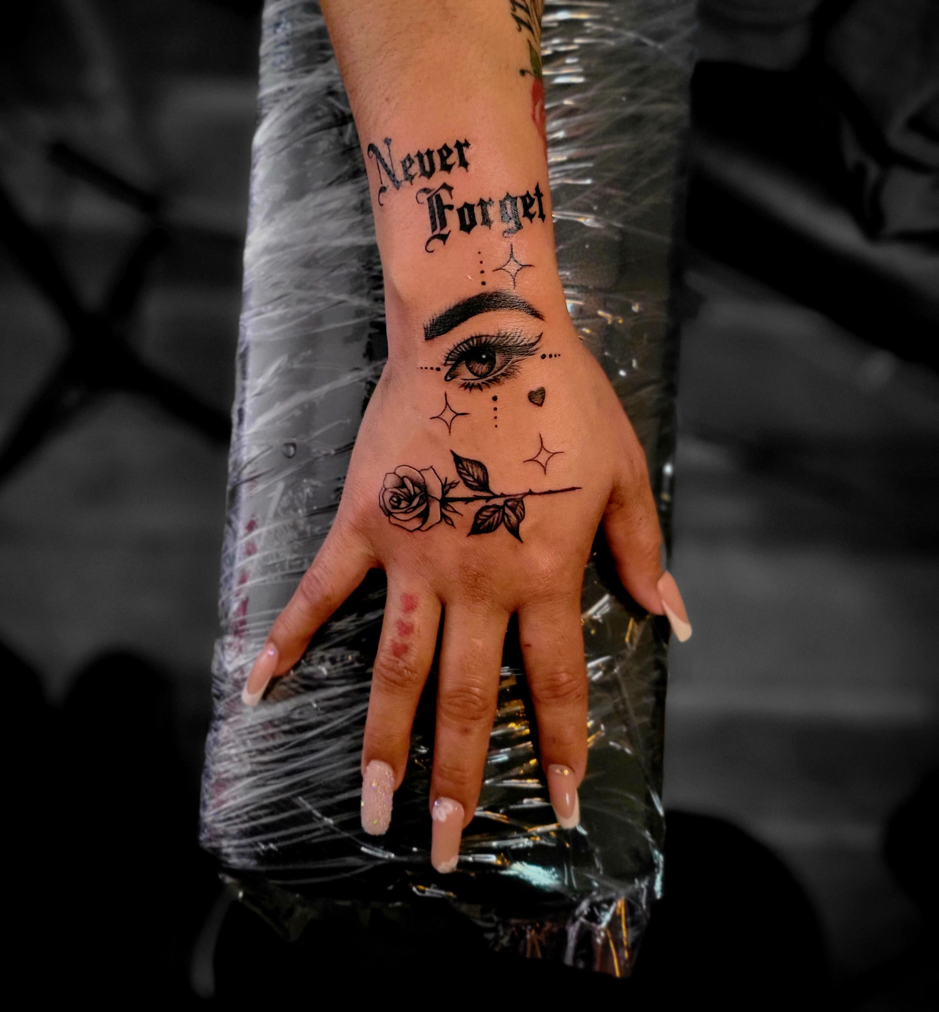 Hand tattoo with Never Forget lettering, an eye, a rose and sparkles