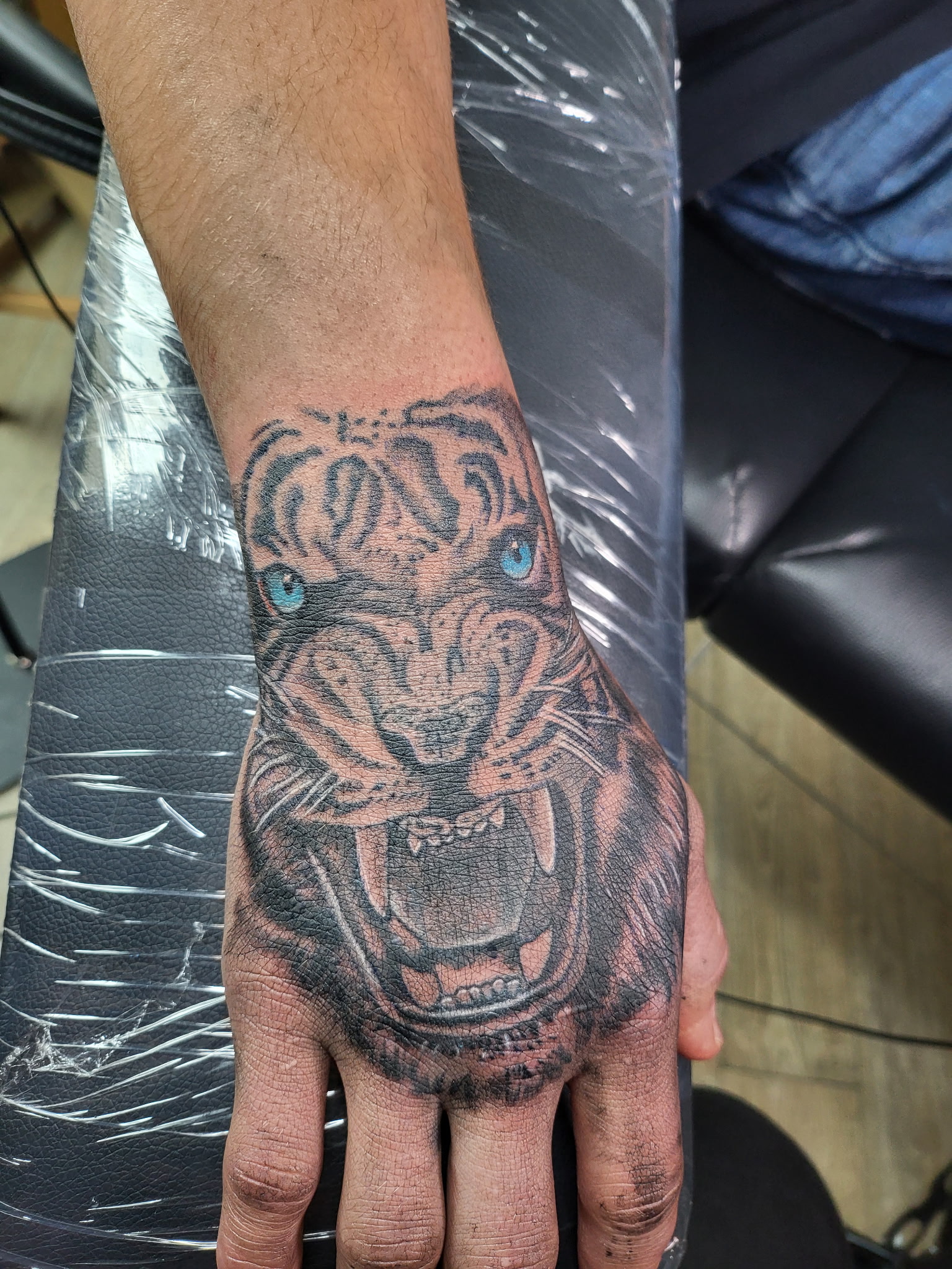 Tiger face tattoo with blue eyes on the back of a hand